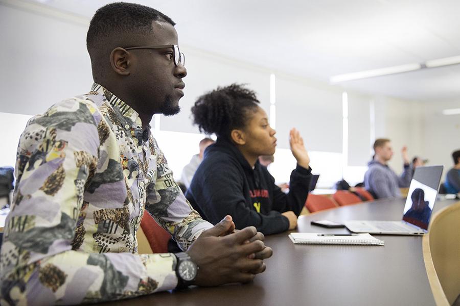 Students sit in a classroom and one student is raising their hand.