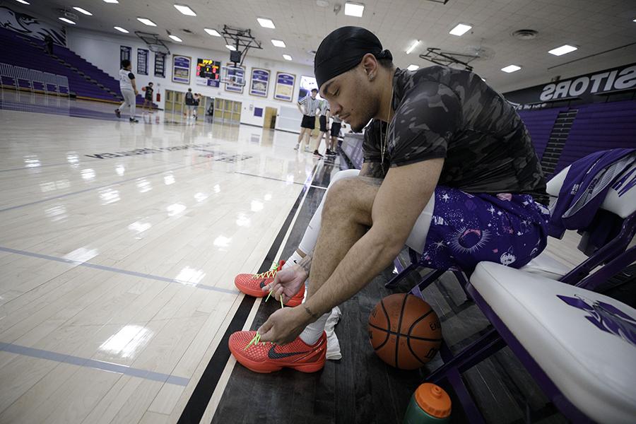 A student laces up their shoes in a basketball gym.