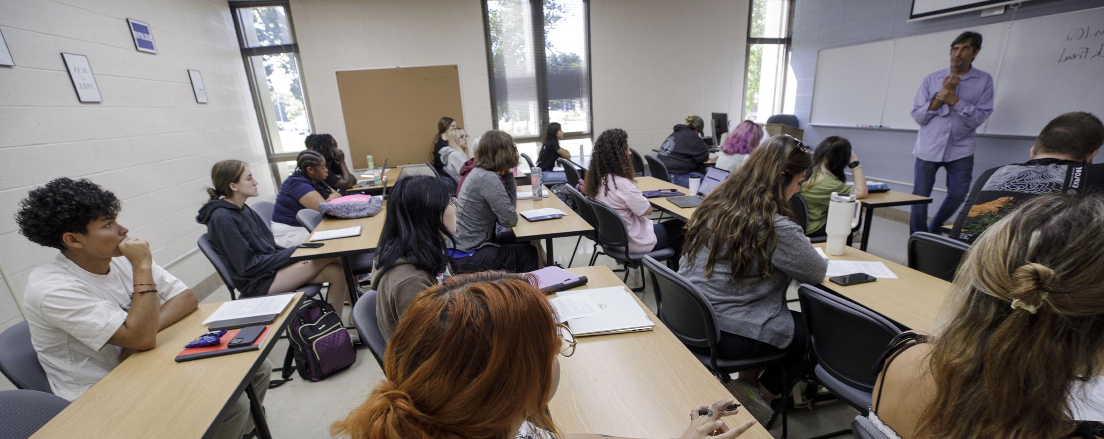 A faculty member teaches at the front of a small class.